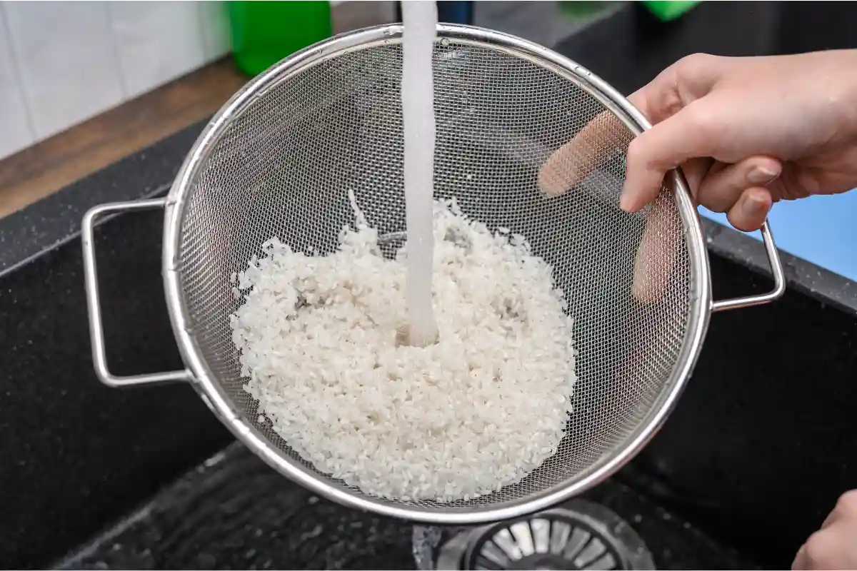 Mano sujetando un colador con arroz blanco