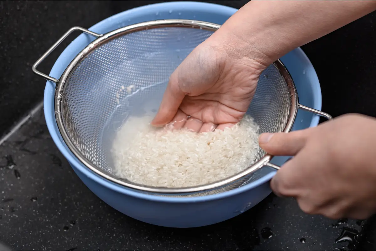 Mano enjuagando arroz blanco en agua