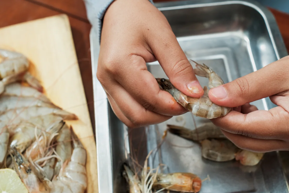 Proceso de las manos de las mujeres pelar la cáscara de los camarones en la mesa de madera. 