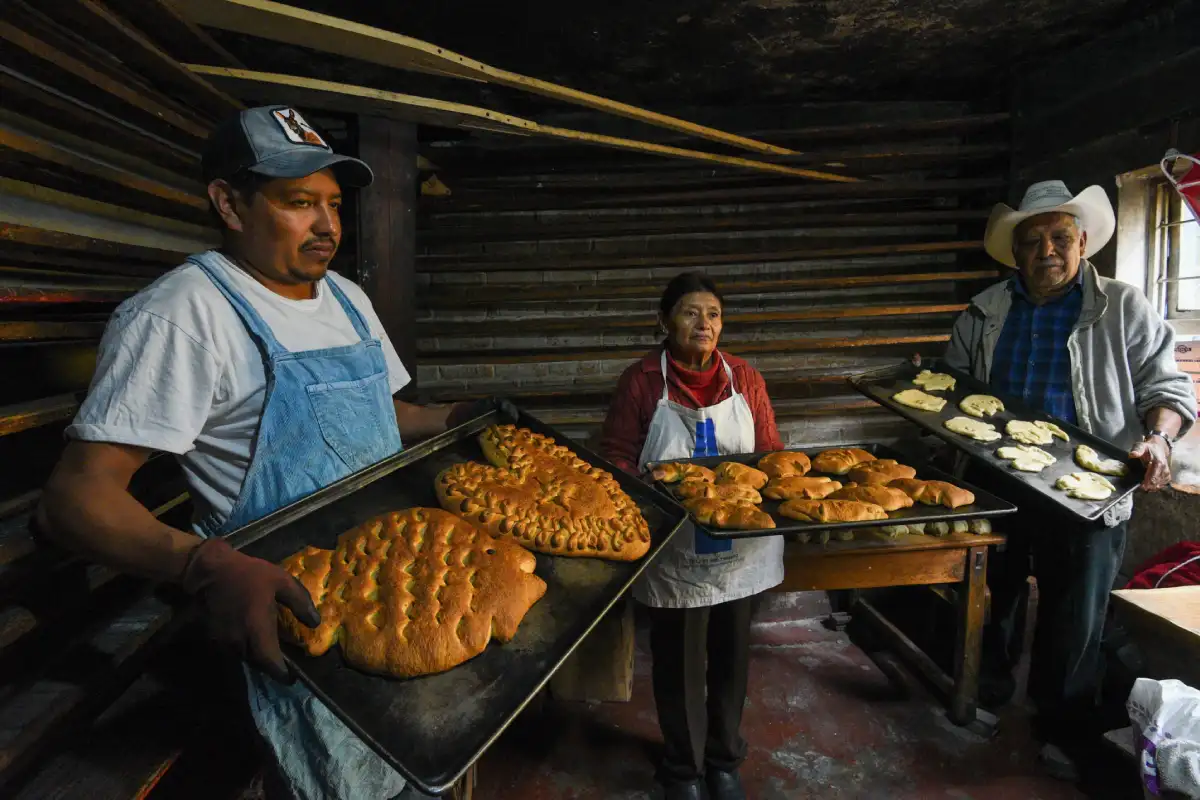 Personas sosteniendo grandes charolas con pan dulce tradicional