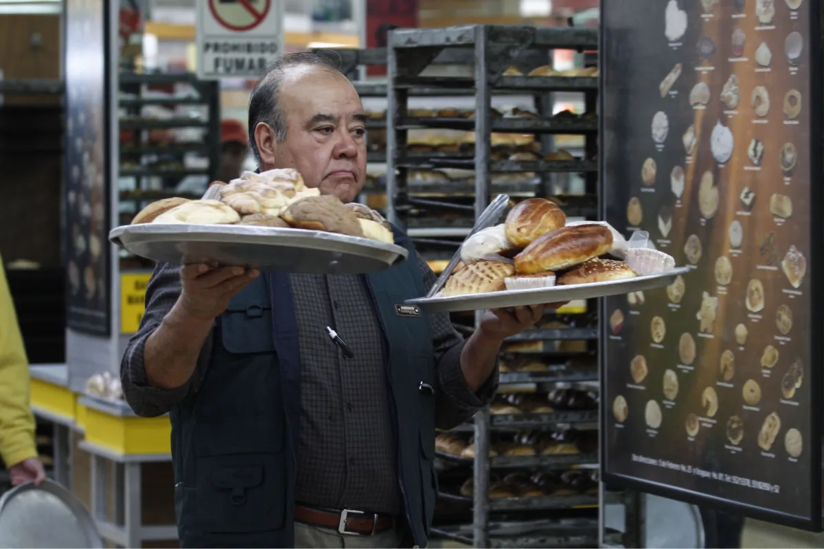 Hombre sostiene dos charolas con piezas de pan dulce