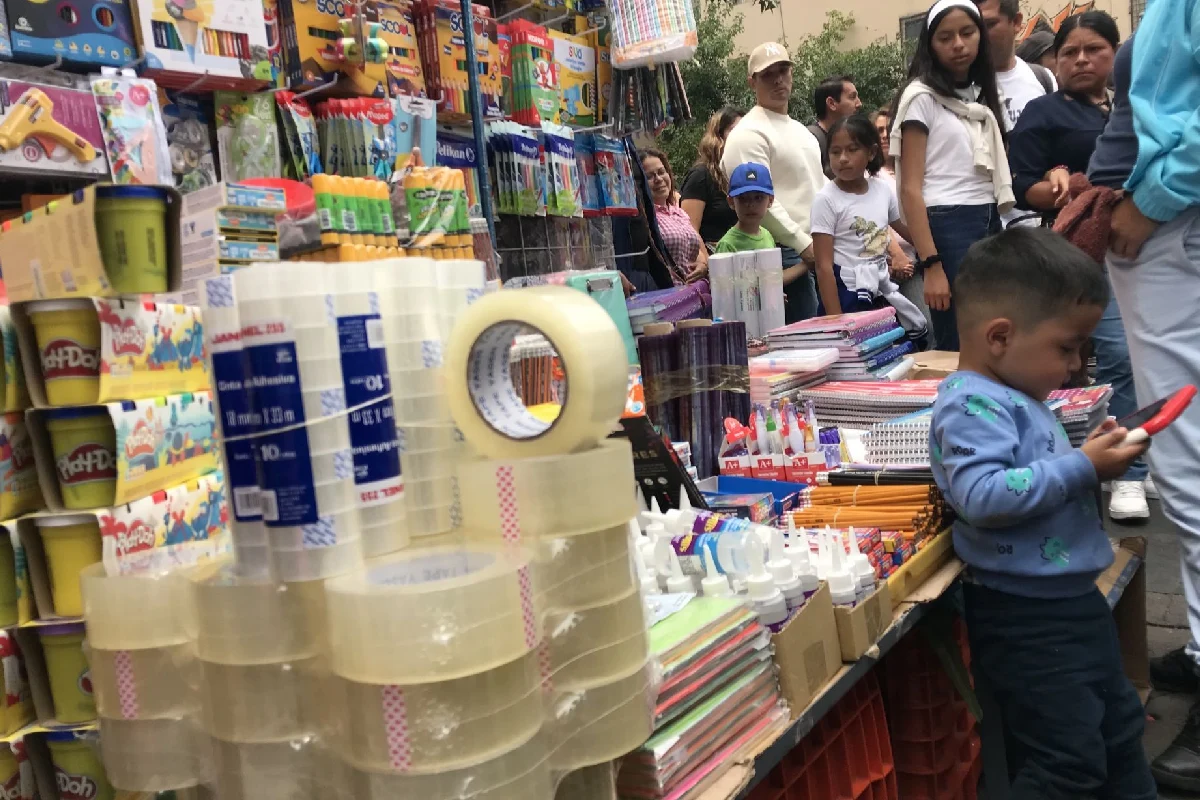 Utiles escolares en un mercado y un niño usando el celular