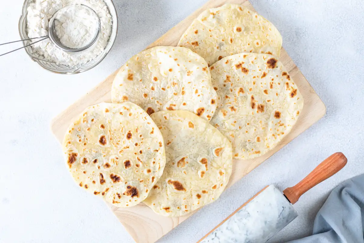 Tortillas de harina sobre un base blanco con un rodillo y harina de trigo