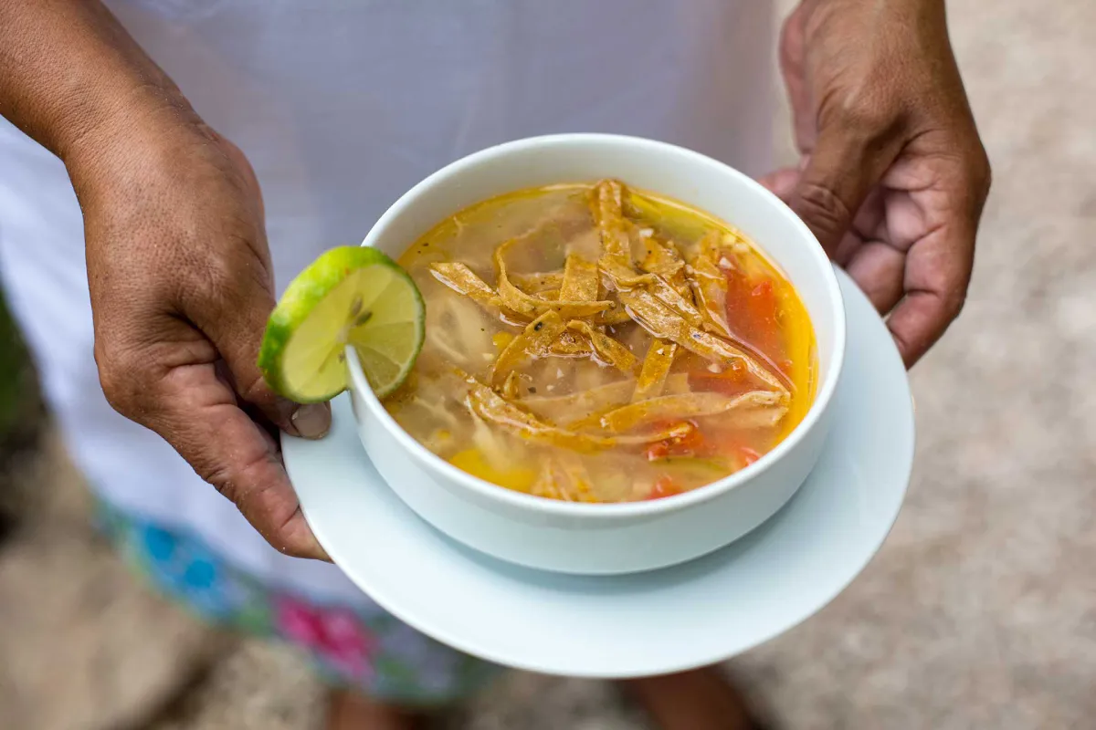 Manos sosteniendo un plato con sopa de lima