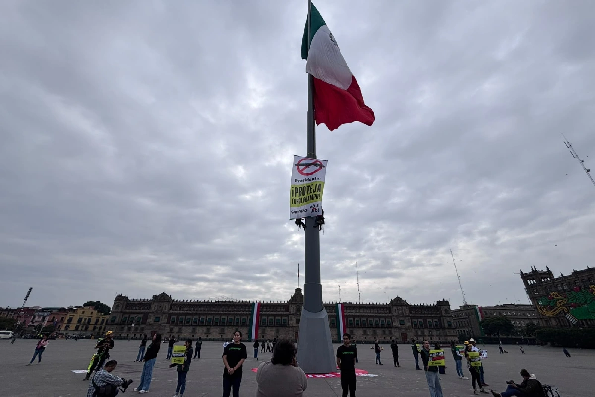 La bandera de México ondeando en el asta del Zócalo de la Ciudad de México, donde activistas de Greenpeace desplegaron una manta con la frase "Presidenta: ¡PROTEJA TOPOLOBAMPO!" sobre la plaza con Palacio Nacional de fondo.