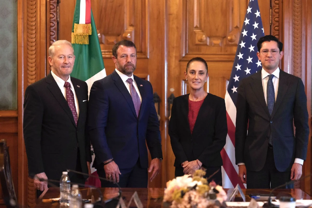 Claudia Sheinbaum posando en fila junto a tres funcionarios vestidos de traje frente a las banderas de México y Estados Unidos dentro de un salón con paneles de madera.