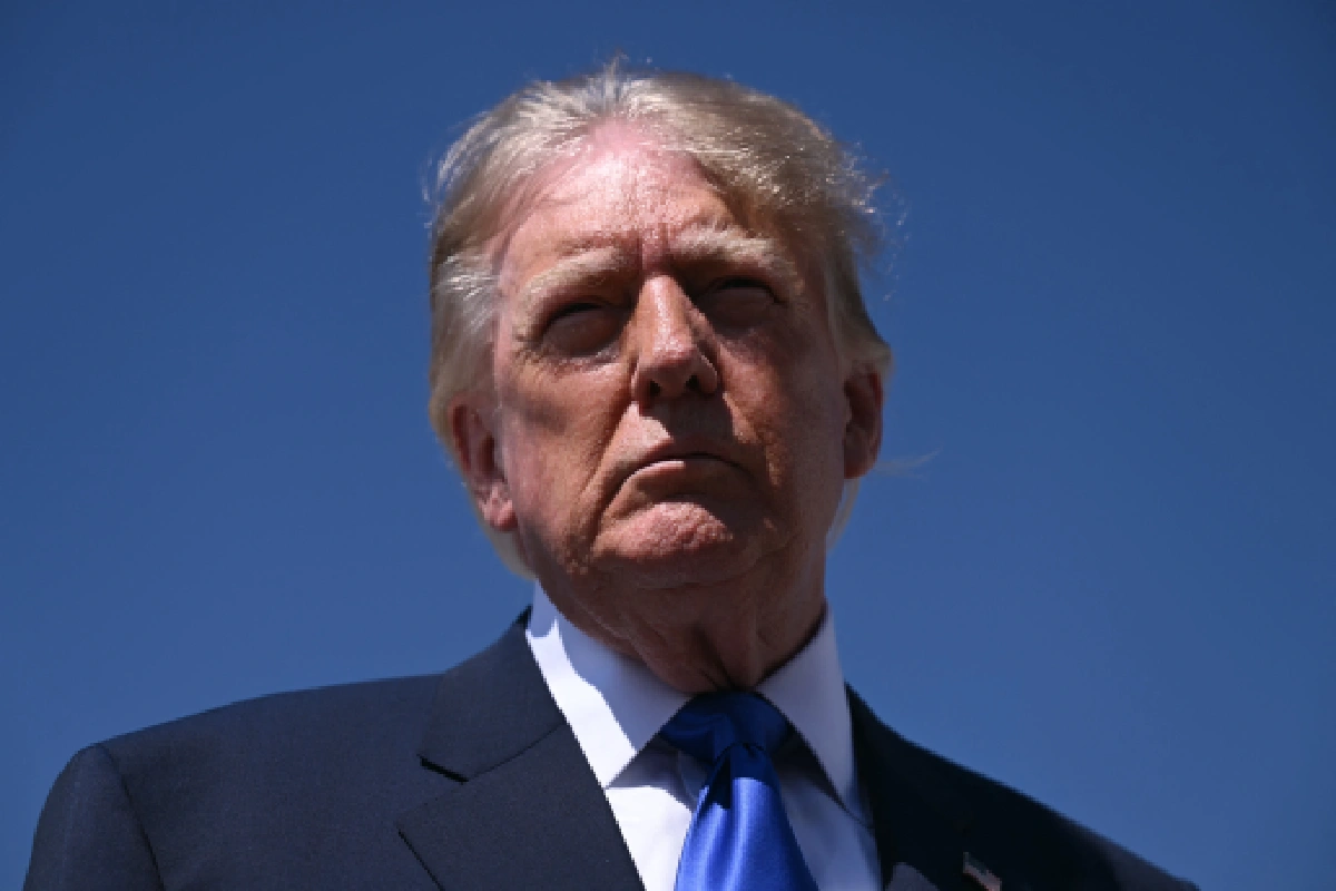 Primer plano en ángulo contrapicado de Donald Trump con rostro serio, vistiendo traje oscuro, camisa blanca y corbata azul sobre un fondo de cielo azul despejado.