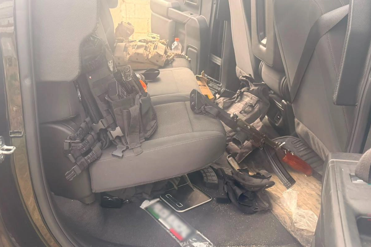 Interior del asiento trasero de un vehículo con chalecos tácticos, porta cargadores, un arma larga tipo rifle de asalto sobre el piso y equipo balístico decomisado.