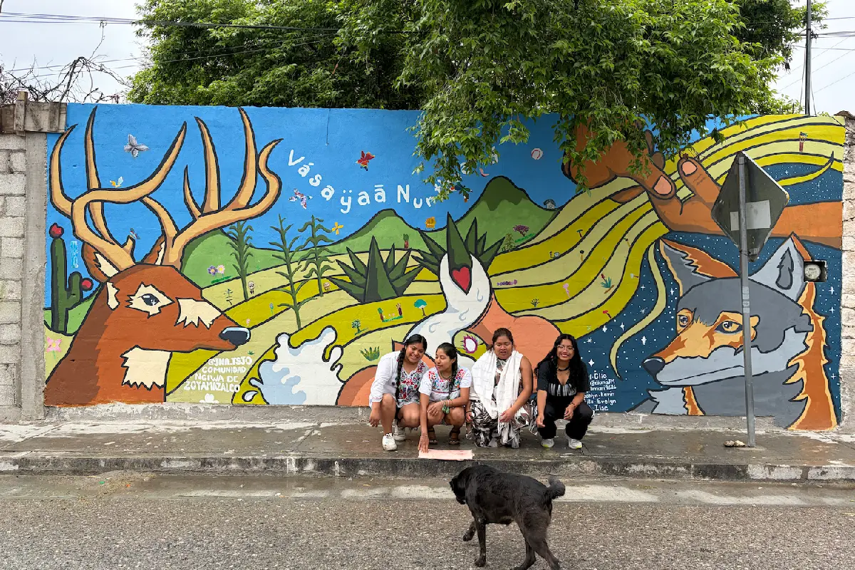 Integrantes del colectivo Jna Tsjo, frente al mural comunitario realizado con las infancias y juventudes de la comunidad de San Mateo Zoyamazalco, con la leyenda "gracias a nuestra tierra" en lengua ngiwa. (Foto: Mongabay Latam | Cortesía Colectivo Jna Tsjo)